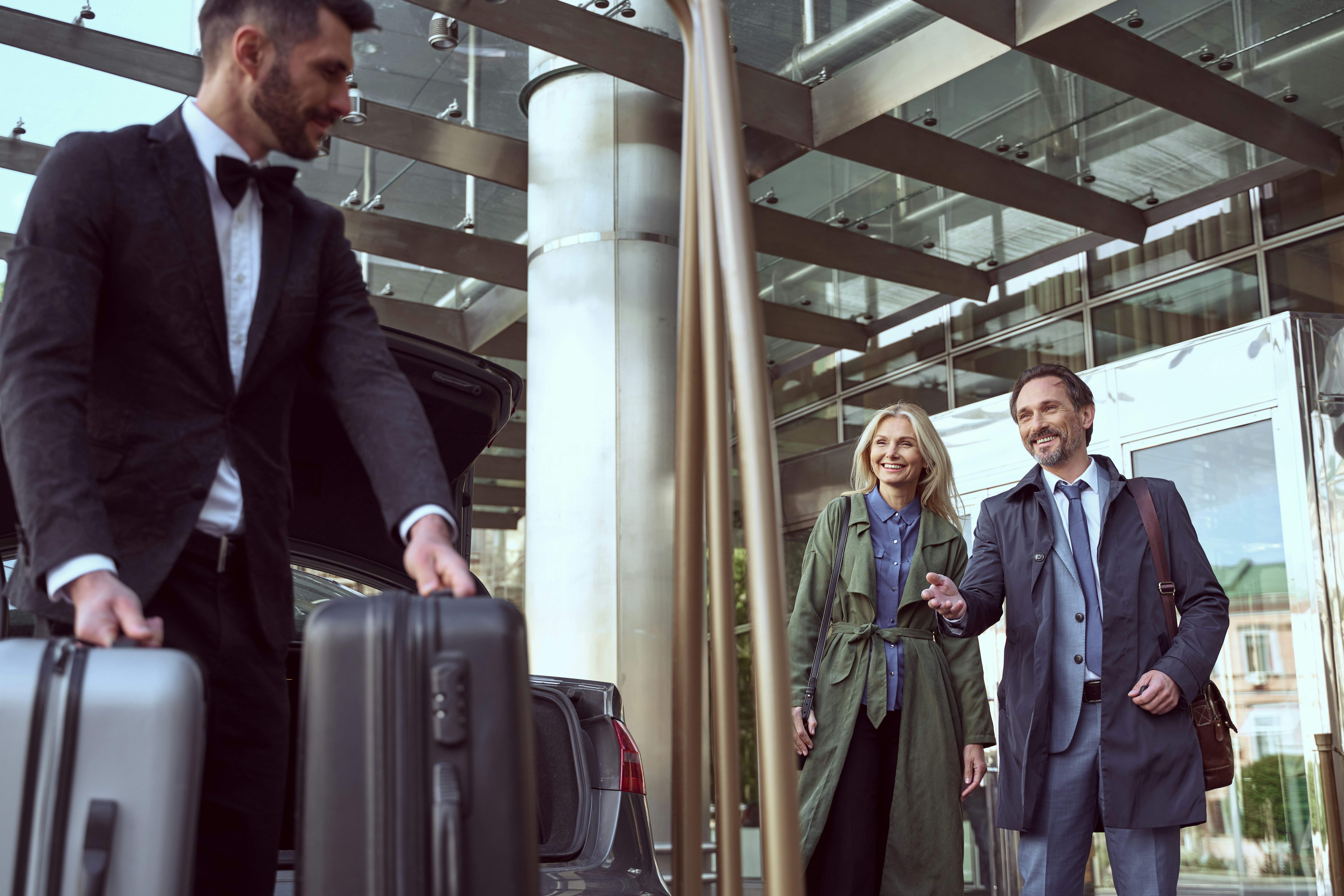 Professional chauffeur assisting with luggage while passengers wait at modern terminal